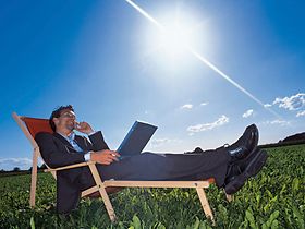 Manager liegt mit Notebook und Handy im Liegestuhl auf Wiese