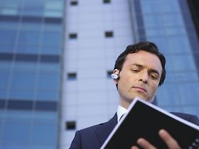 Manager steht mit Timeplaner vor Buerogebaeude