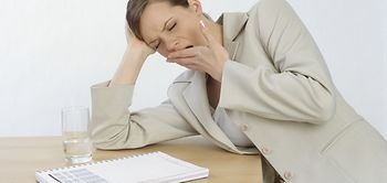 Managerin sitzt muede und gaehnend am Schreibtisch