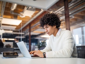Side view of young businessman using laptop in office. Male professional sitting at conference table