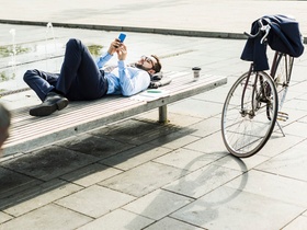 Young businessman lying on bench, working