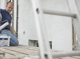 Mann auf Gerüst streicht Hauswand