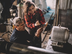 Two people, senior man nad young woman, repairing electric motor in workshop.