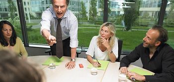 Mann gestikuliert wütend an Konferenztisch mit Kollegen