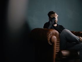 Mann hält sich auf einem Sessel sitzend den Kopf