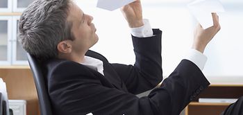 Mann im Anzug sitzt am Schreibtisch und baut Papierflieger