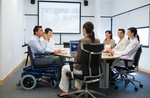 Mann im Rollstuhl sitzt mit Kollegen an Besprechungstisch