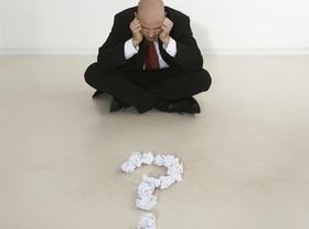 Mann im Schneidersitz hat Fragezeichen aus Papierballen vor sich