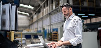 Mann in Lagerhalle mit Laptop