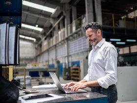 Mann in Lagerhalle mit Laptop