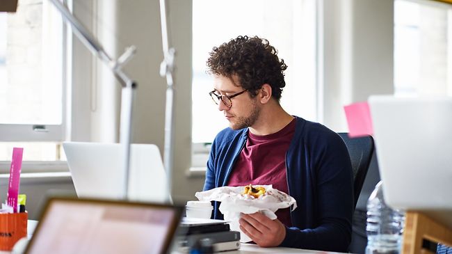 Mann isst Frühstück am Tisch vorm PC