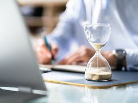 Mann Laptop Schreibtisch Stundenglass Unterlagen