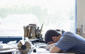 Mann legt Kopf auf überfüllten Schreibtisch