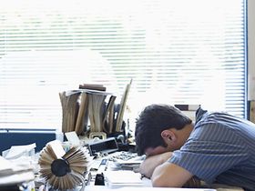 Mann legt Kopf auf überfüllten Schreibtisch