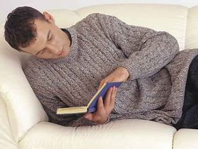 Mann liegt auf Sofa, liest ein Buch