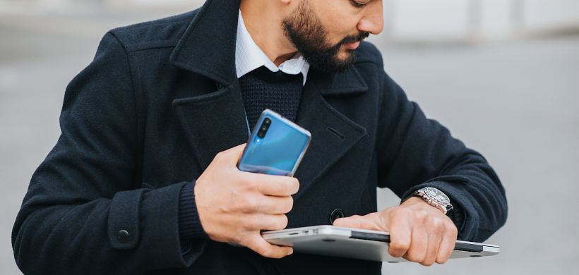 Mann mit Laptop und Handy schaut auf seine Uhr