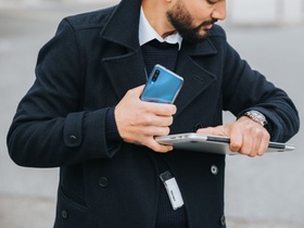 Mann mit Laptop und Handy schaut auf seine Uhr