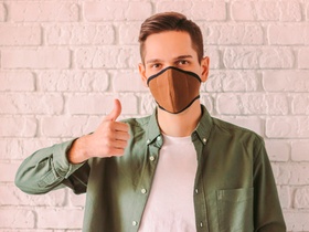 Young stylish hipster in protective mask on face show thumb up gesture. Prevention of coronavirus CO