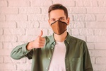Young stylish hipster in protective mask on face show thumb up gesture. Prevention of coronavirus CO