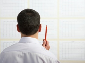 Mann mit Stift planend vor Tafel mit Papieren