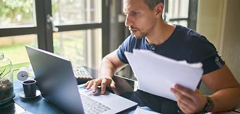 Mann prüft Steuerunterlagen am Laptop im Homeoffice