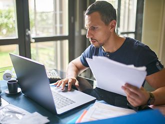 Mann prüft Steuerunterlagen am Laptop im Homeoffice