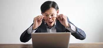 Mann schaut durch Brille auf Laptop