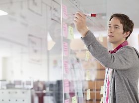 Mann schreibt auf Post-its an Glaswand