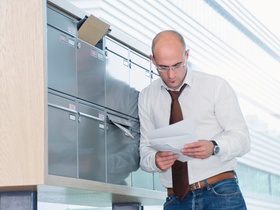 Mann sieht sich seine Post am Briefkasten an
