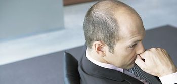 Mann sitzt an Tisch und hält seine Faust vor den Mund