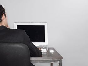 Mann sitzt an Tisch vor Computerbildschirm