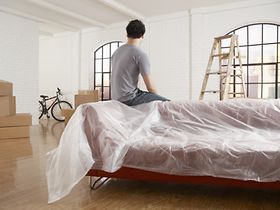 Mann sitzt auf eingepackter Couch und schaut auf Kartons