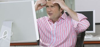 Mann sitzt im Buero gestresst vor Computer