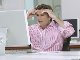 Mann sitzt im Buero gestresst vor Computer