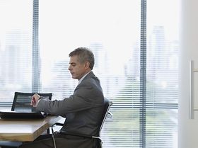 Mann sitzt im Konferenzsaal, schaut auf die Uhr