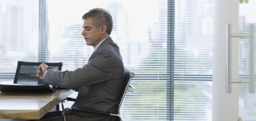 Mann sitzt im Konferenzsaal, schaut auf die Uhr