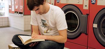 Mann sitzt im Waschsalon, liest ein Buch