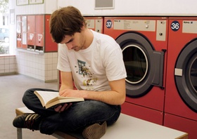 Mann sitzt im Waschsalon, liest ein Buch