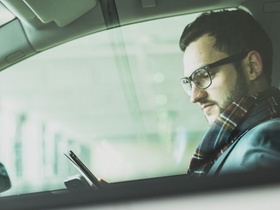 Mann sitzt in Auto und blickt auf Smartphone