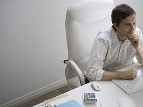 Mann sitzt lächelnd vor Laptop Maus Taschenrechner