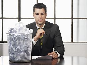 Mann sitzt mit vollem Papierkorb an Schreibtisch