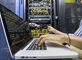 Mann sitzt neben Server und tippt in sein Laptop