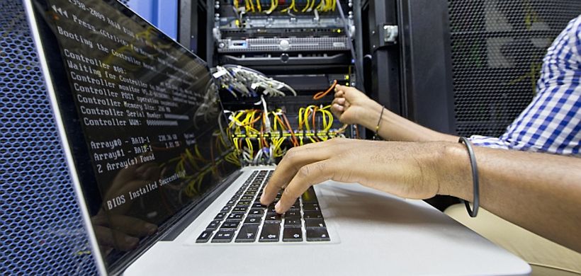 Mann sitzt neben Server und tippt in sein Laptop
