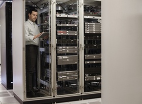 Mann steht in Serverraum und tippt etwas in sein Tablet