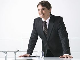 Mann steht laechelnd im Buero an Konferenztisch