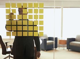 Mann steht vor Glaswand mit quadratisch aufgeklebten Post its