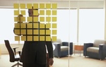 Mann steht in Büro vor Glaswand mit quadratischen aufgeklebten Post its