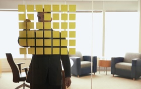 Mann steht in Büro vor Glaswand mit quadratischen aufgeklebten Post its