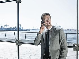 Mann telefoniert mit Handy in Buerogebaeude vor Glasfront, Hafen 