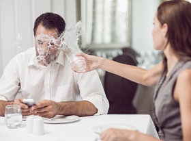 Mann tippt am Handy Frau schüttet ihm ein Glas Wasser ins Gesicht